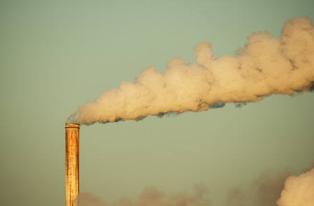 old rusty smokestack with plume of smoke lit by early morning light