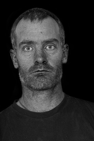portrait of a rugged grizzled middle aged man with black t-shirt on black background processed to...