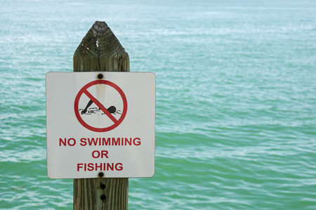 no swimming or fishing sign on a post with out of focus water behind itの写真素材