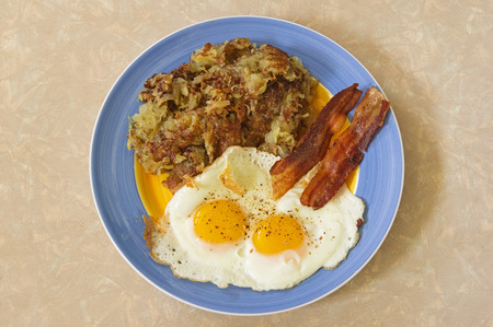 hearty breakfast plate with hash browns two eggs and baconの写真素材