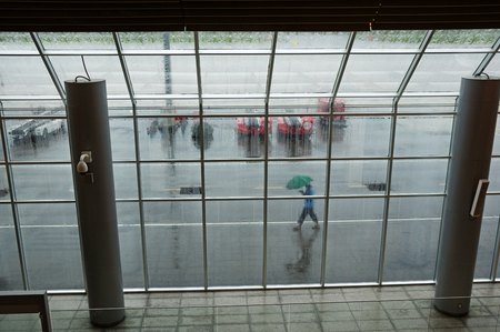 looking out through an airport window on a rainy day with a person walking by outside with umbrellaの写真素材