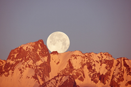 a full moon setting over Mount Humphreys mountain as the first light hits the summitの写真素材
