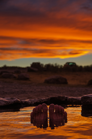 toes and feet poking out of a hot spring at sunset with reflection in the water and selective focusの写真素材