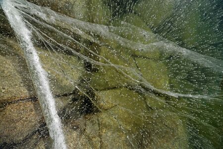 view down into cracked ice on a frozen mountain lake with rocks on the bottomの写真素材