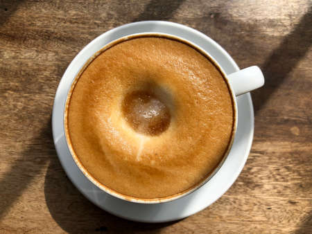 A cup of coffee on a wooden table with sunlight. Top view.