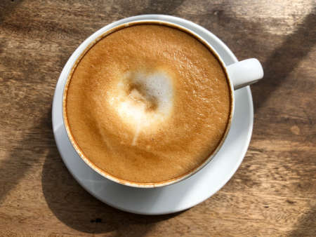 Cup of cappuccino coffee on wooden table, top view