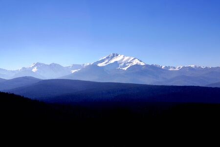 Wide view of a section of the snow-capped rocky mountains with trees in the foreground