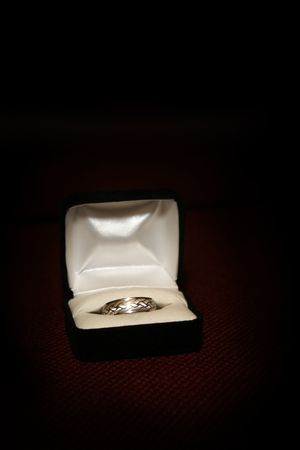 Wedding ring in a ring box on a red textured surface with a spotlight effect