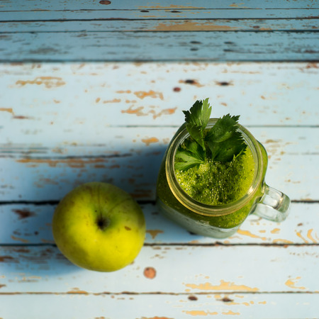 Healthy detox green apple and vegetables juice in Mason jar with celery on the top. It serves on wooden blue vintage backgroundの写真素材