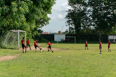 BADUNG,BALI/INDONESIA-APRIL 05 2019: Elementary student in Bali play football or soccer on the field with red jersey.のeditorial素材