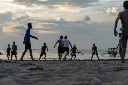 BADUNG,BALI/INDONESIA-APRIL 02 2019: Asian Teenager play football or soccer at Kuta beach with sunset or golden hours background.The sky is cloudy and some traditional boat which is called jukung, anchored thereのeditorial素材