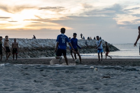 BADUNG,BALI/INDONESIA-APRIL 02 2019: Asian Teenager play football or soccer at Kuta beach with sunset or golden hours background.The sky is cloudy and some traditional boat which is called jukung, anchored thereのeditorial素材