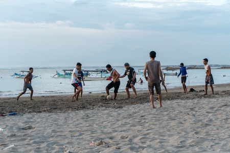 BADUNG,BALI/INDONESIA-APRIL 02 2019: Asian Teenager play football or soccer at Kuta beach with sunset or golden hours background.The sky is cloudy and some traditional boat which is called jukung, anchored thereのeditorial素材