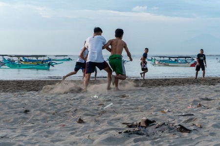BADUNG,BALI/INDONESIA-APRIL 02 2019: Asian Teenager play football or soccer at Kuta beach with sunset or golden hours background.The sky is cloudy and some traditional boat which is called jukung, anchored thereのeditorial素材