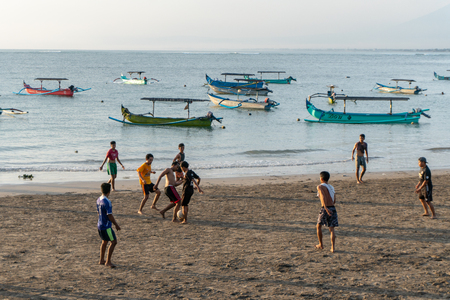 BADUNG,BALI/INDONESIA-APRIL 02 2019: Asian Teenager play football or soccer at Kuta beach with sunset or golden hours background. Some traditional boat which is called jukung, anchored thereのeditorial素材