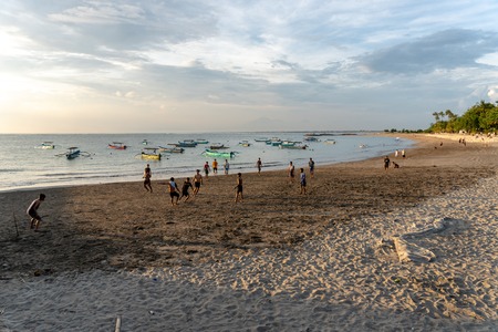 BADUNG,BALI/INDONESIA-APRIL 02 2019: Asian Teenager play football or soccer at Kuta beach with sunset or golden hours background.The sky is cloudy and some traditional boat which is called jukung, anchored thereのeditorial素材