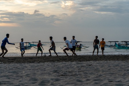 BADUNG,BALI/INDONESIA-APRIL 02 2019: Asian Teenager play football or soccer at Kuta beach with sunset or golden hours background.The sky is cloudy and some traditional boat which is called jukung, anchored thereのeditorial素材