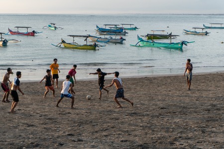 BADUNG,BALI/INDONESIA-APRIL 02 2019: Asian Teenager play football or soccer at Kuta beach with sunset or golden hours background.The sky is cloudy and some traditional boat which is called jukung, anchored thereのeditorial素材