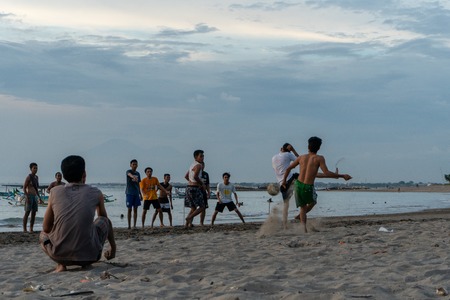 BADUNG,BALI/INDONESIA-APRIL 02 2019: Asian Teenager play football or soccer at Kuta beach with sunset or golden hours background.The sky is cloudy and some traditional boat which is called jukung, anchored thereのeditorial素材
