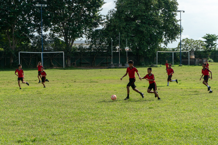 BADUNG,BALI/INDONESIA-APRIL 05 2019: Elementary student in Bali play football or soccer on the field with red jersey.のeditorial素材