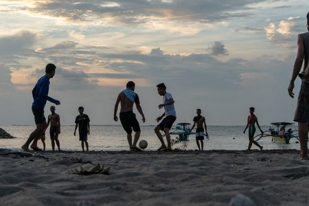 BADUNG,BALI/INDONESIA-APRIL 02 2019: Asian Teenager play football or soccer at Kuta beach with sunset or golden hours background.The sky is cloudy and some traditional boat which is called jukung, anchored thereのeditorial素材