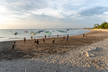 BADUNG,BALI/INDONESIA-APRIL 02 2019: Asian Teenager play football or soccer at Kuta beach with sunset or golden hours background.The sky is cloudy and some traditional boat which is called jukung, anchored thereのeditorial素材