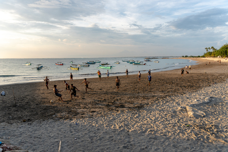BADUNG,BALI/INDONESIA-APRIL 02 2019: Asian Teenager play football or soccer at Kuta beach with sunset or golden hours background.The sky is cloudy and some traditional boat which is called jukung, anchored thereのeditorial素材