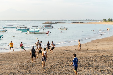 BADUNG,BALI/INDONESIA-APRIL 02 2019: Asian Teenager play football or soccer at Kuta beach with sunset or golden hours background. Some traditional boat which is called jukung, anchored thereのeditorial素材