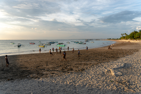 BADUNG,BALI/INDONESIA-APRIL 02 2019: Asian Teenager play football or soccer at Kuta beach with sunset or golden hours background.The sky is cloudy and some traditional boat which is called jukung, anchored thereのeditorial素材