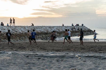 BADUNG,BALI/INDONESIA-APRIL 02 2019: Asian Teenager play football or soccer at Kuta beach with sunset or golden hours background.The sky is cloudy and some traditional boat which is called jukung, anchored thereのeditorial素材