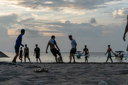 BADUNG,BALI/INDONESIA-APRIL 02 2019: Asian Teenager play football or soccer at Kuta beach with sunset or golden hours background.The sky is cloudy and some traditional boat which is called jukung, anchored thereのeditorial素材