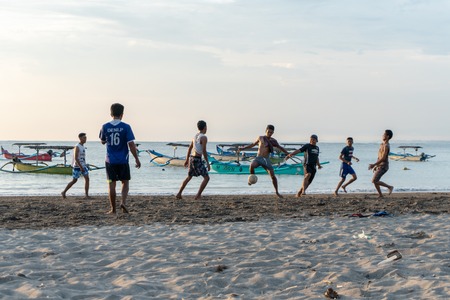 BADUNG,BALI/INDONESIA-APRIL 02 2019: Asian Teenager play football or soccer at Kuta beach with sunset or golden hours background.The sky is cloudy and some traditional boat which is called jukung, anchored thereのeditorial素材