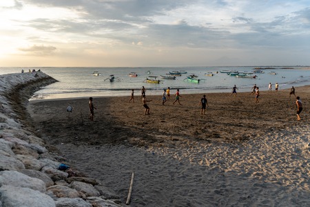 BADUNG,BALI/INDONESIA-APRIL 02 2019: Asian Teenager play football or soccer at Kuta beach with sunset or golden hours background.The sky is cloudy and some traditional boat which is called jukung, anchored thereのeditorial素材