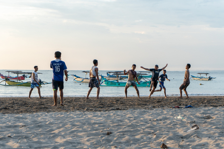BADUNG,BALI/INDONESIA-APRIL 02 2019: Asian Teenager play football or soccer at Kuta beach with sunset or golden hours background.The sky is cloudy and some traditional boat which is called jukung, anchored thereのeditorial素材