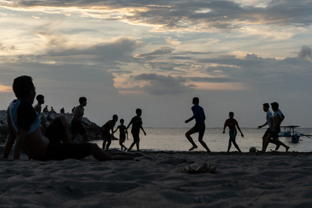 BADUNG,BALI/INDONESIA-APRIL 02 2019: Asian Teenager play football or soccer at Kuta beach with sunset or golden hours background.The sky is cloudy and some traditional boat which is called jukung, anchored thereのeditorial素材