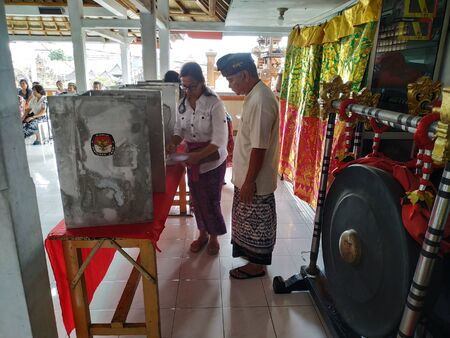 BALI/INDONESIA-APRIL 17 2019: Balinese people vote for the president and parliament 2019. They go to the polling stations using traditional clothes. A person with disability get helped from officerのeditorial素材
