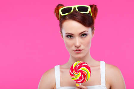 Portrait of beautiful  merry redheaded girl with a large candy on a pink backgroundの写真素材