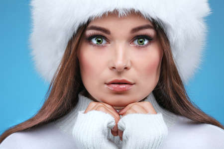 Beautiful merry sexual girl in a white fur cap and warm clothes on a blue backgroundの写真素材