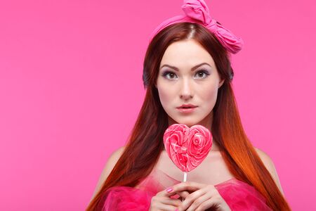 Portrait of beautiful  merry redheaded girl with a large candy on a pink backgroundの写真素材