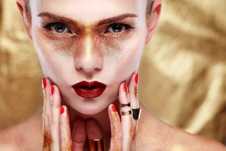 Closeup portrait of sexy  young woman with beautiful blue eyes and red lips on gold  backgroundの写真素材