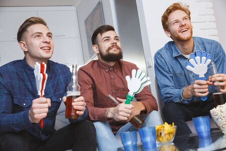 Men watching sport on tv together at home holding noisemakersの写真素材