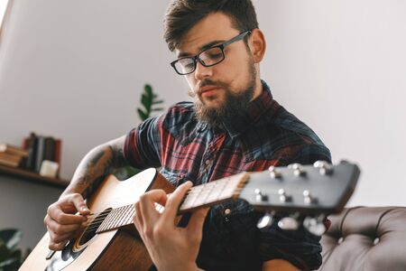 Young guitarist hipster at home with guitar sitting playing concentrated close-upの写真素材