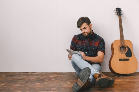 Young guitarist hipster at home with guitar sitting writing melodyの写真素材