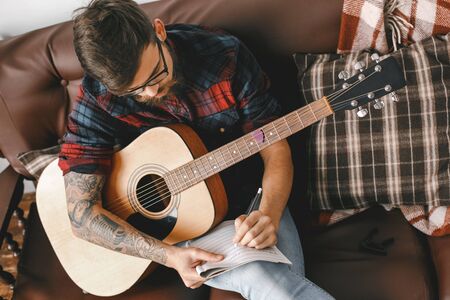 Young guitarist hipster at home with guitar sitting writing notes top view