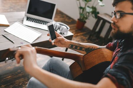 Young guitarist hipster at home tuning guitar close-upの写真素材