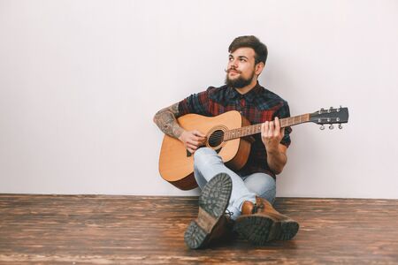 Young guitarist hipster at home sitting on the floor playing guitar thinkingの写真素材