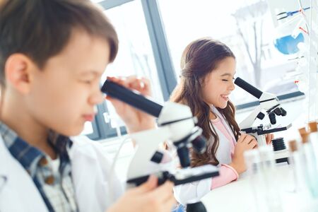 Little kids learning chemistry in school laboratory looking in microscopesの写真素材