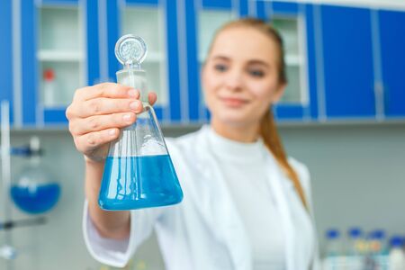 Young chemistry teacher in school laboratory work standing holding bulb close-upの写真素材