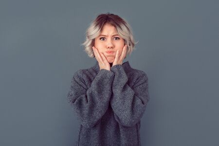 Young woman in a grey sweater studio picture isolated on grey background grimaseの写真素材