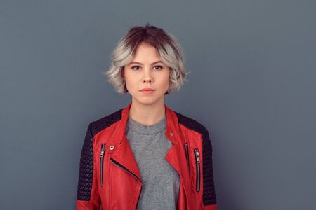 Young woman standing in leather jacket isolated on grey wall thoughtfulの写真素材